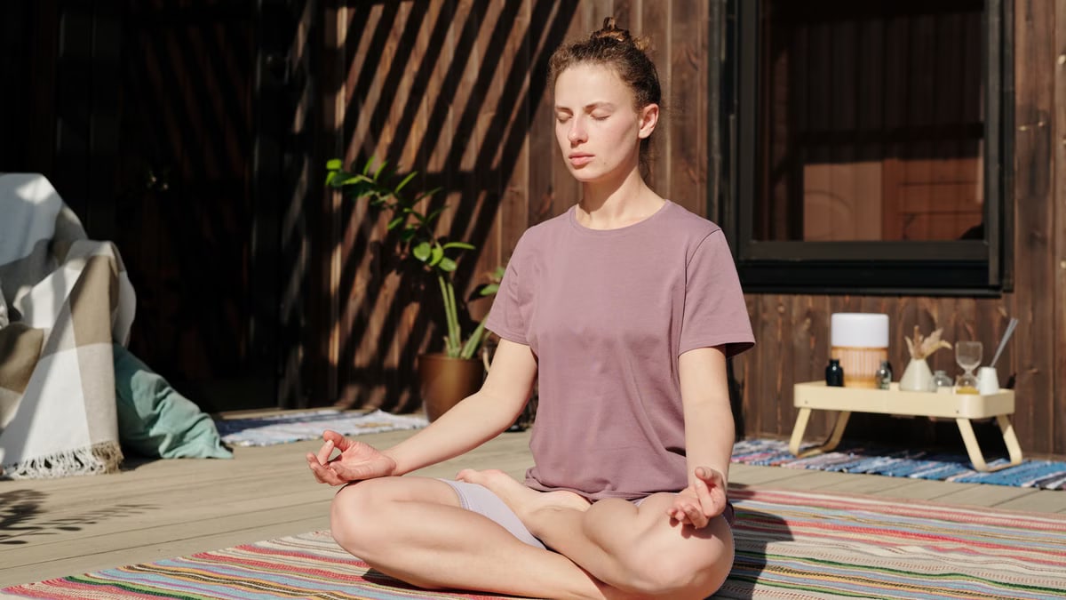 Woman practicing meditation in lotus pose on a sunny outdoor deck.
